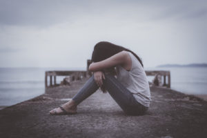 A woman sits alone on a dock while hiding her head. Learn how CBT therapy in Grand Rapids, MI can offer support. A CBT therapist in Grand Rapids, MI can offer cognitive behavioral therapy in Grand Rapids, MI and other services.