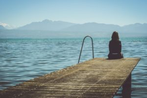 A woman sits alone at the end of a dock while looking out at the water. Depression treatment in Kent County, MI can help you overcome isolation and other symptoms. Learn more about online depression therapy in Kent County, MI by contacting a depression therapist in Kent County, MI for more info.