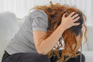 An upset woman holds her head while hunched over. This could represent the pain EMDR therapy in Grand Rapids, MI can offer support addressing. Learn more about online EMDR therapy in Kent County, MI and other services by contacting an EMDR therapist in Grand Rapids, MI.