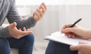 A person gestures with their hands as a person writes notes on a clipboard. This could represent a grief counselor in Grand Rapids, MI meeting with a client. Learn how grief counseling in Grand Rapids, MI can offer support from the comfort of home with online greif counseling in Kent County, 