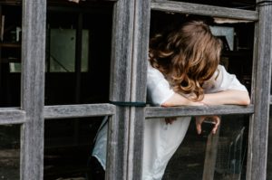 A woman leans on a wooden frame as she hides her face. This could represent the isolation anxiety treatment in Grand Rapids, Mi can address. Learn more about about online anxiety treatment in Kent County, MI by contacting an online anxiety therapist in Grand Rapids, MI today. 