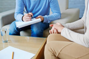 A close up of a person taking notes on a clipboard while sitting across from another person. This could represent the support an anxiety therapist in Grand Rapids, MI can offer. Learn more about how anxiety treatment in Grand Rapids, MI can occur from your own home today.