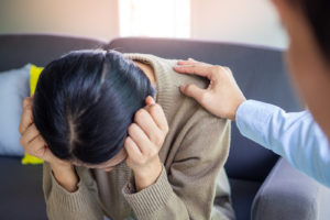 An upset woman receives a supportive hand on the shoulder. Learn more about online therapy in Grand Rapids, MI and CBT therapy in Grand Rapids, MI today. We offer therapy that takes insurance in Grand Rapids, MI and more.